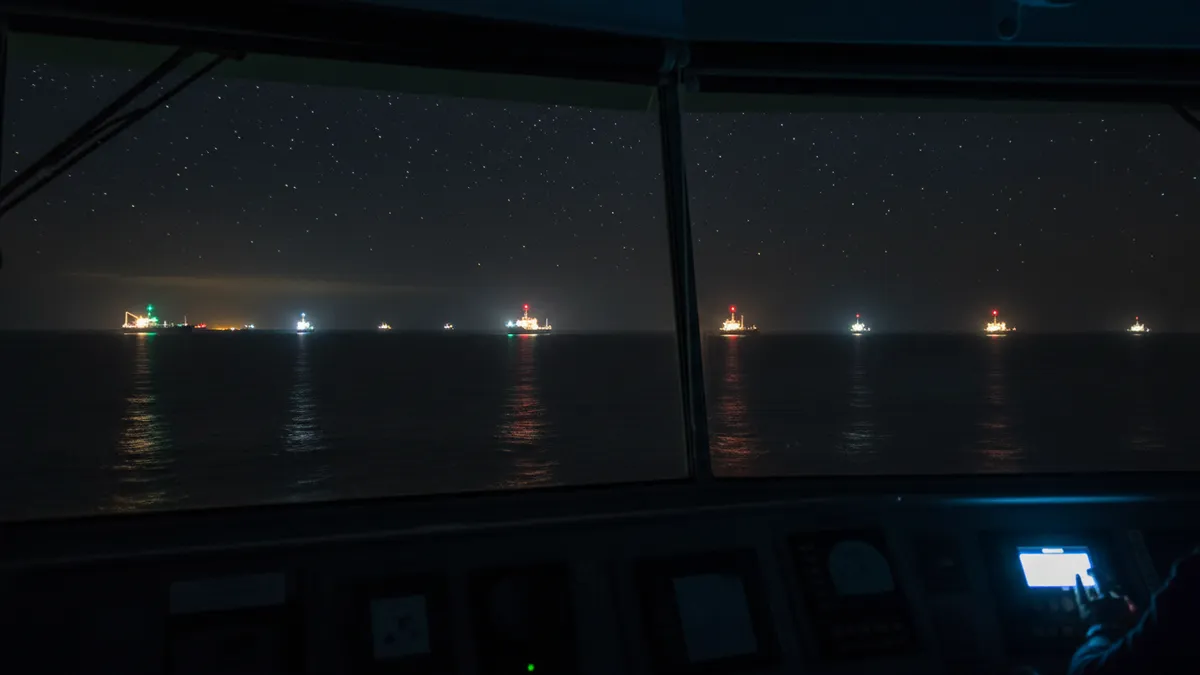 Plusieurs navires de nuit en mer, feux de navigation colorés visibles à l'horizon, vue depuis la passerelle d'un navire au quart
