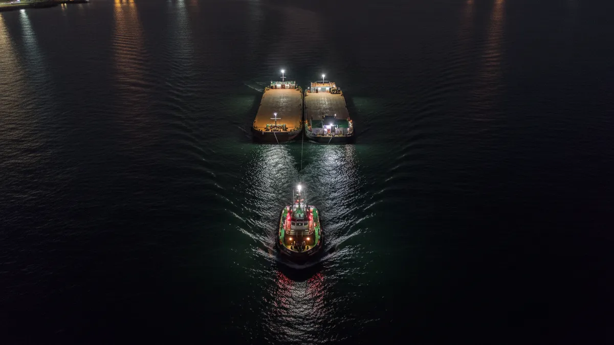 Remorqueur de nuit en mer avec deux feux de mât blancs superposés et un feu jaune de remorquage au-dessus du feu de poupe, remorqué visible à l'arrière